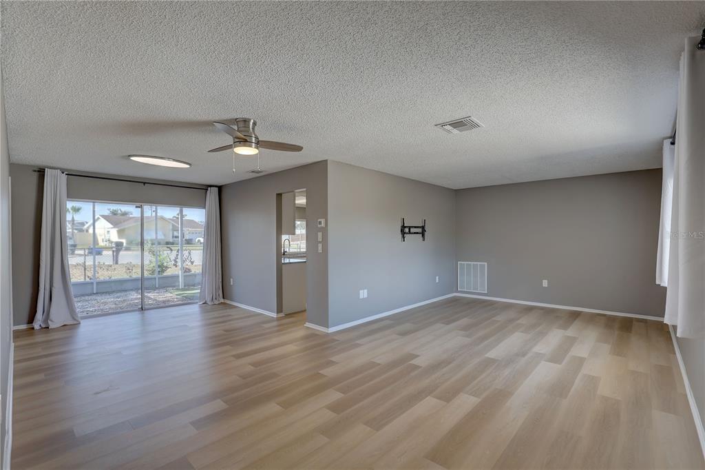 A living room features light wood-look flooring, gray walls, a ceiling fan, and sliding glass doors — 3718 PENRICK DRIVE, HOLIDAY, FL