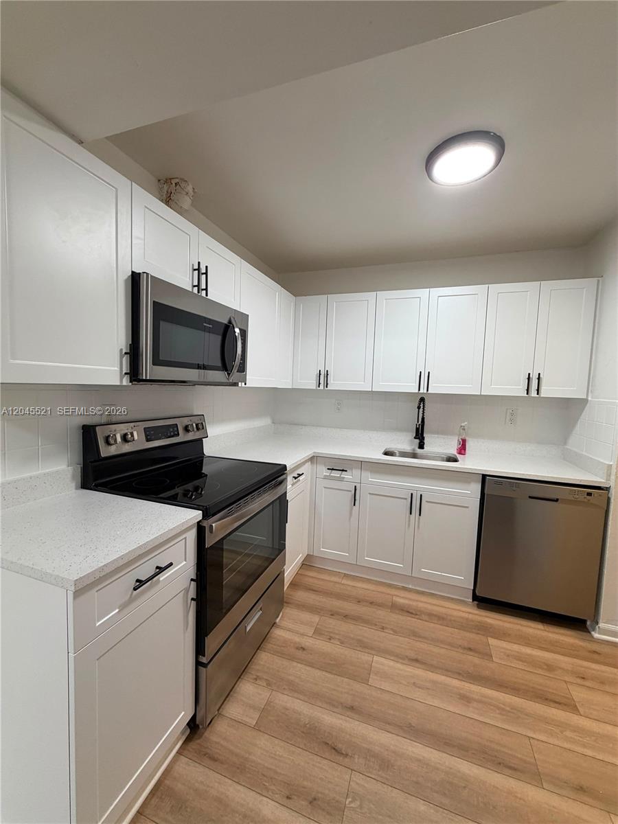 A kitchen features white cabinets, stainless steel appliances, light countertops, and wood-look flooring — 2551 NW 26th St, Sunrise FL 33313, SUNRISE, FL
