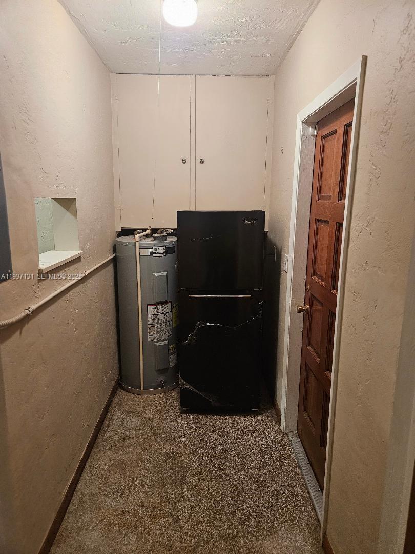 A utility room contains a water heater, a black refrigerator, and cabinets on carpeted flooring — 5842 Harding St # R, Hollywood FL 33021, HOLLYWOOD, FL