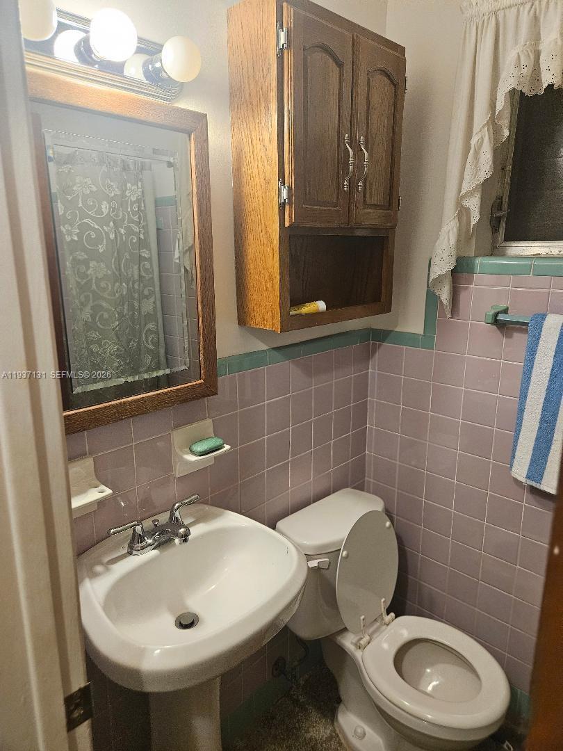 A small bathroom features a pedestal sink, a toilet, and pink wall tiles — 5842 Harding St # R, Hollywood FL 33021, HOLLYWOOD, FL
