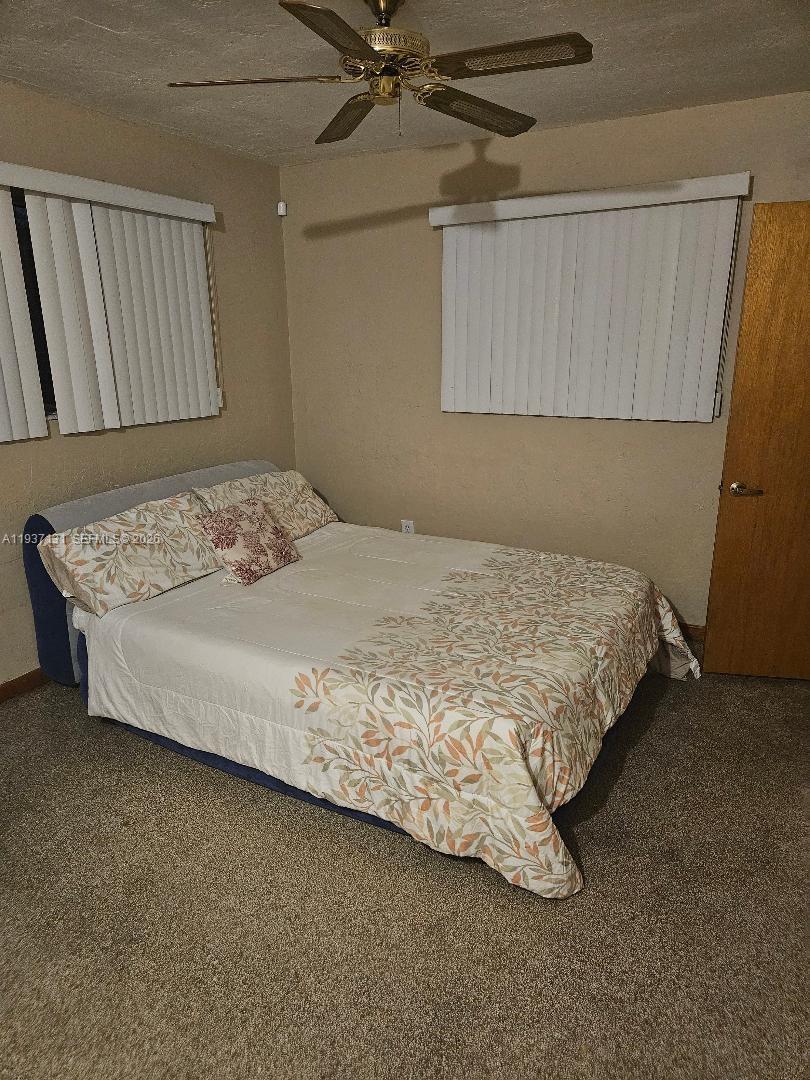 A bedroom features a bed with a patterned comforter, beige walls, and a ceiling fan — 5842 Harding St # R, Hollywood FL 33021, HOLLYWOOD, FL