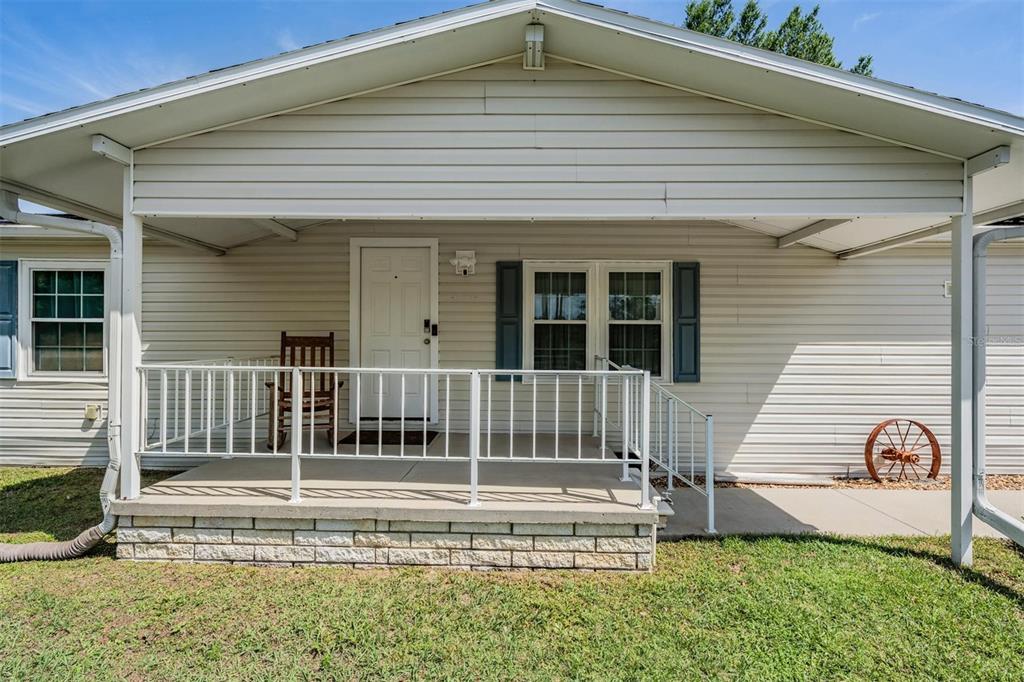 A covered front porch with a white railing sits in front of a light-sided house — 13544 KENT BRADLEY STREET, DADE CITY, FL