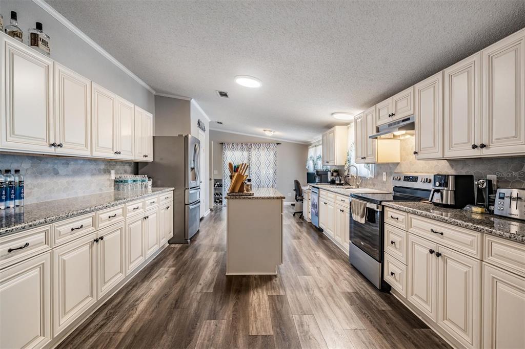 A kitchen with white cabinets, granite countertops, stainless steel appliances, and wood-look flooring — 13544 KENT BRADLEY STREET, DADE CITY, FL