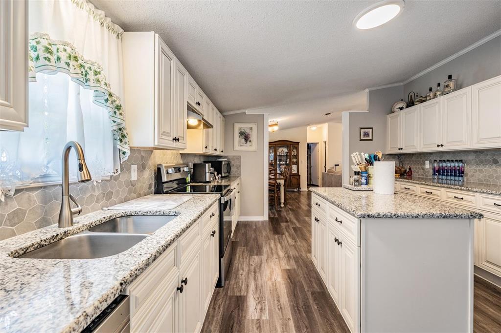 A kitchen features white cabinets, granite countertops, a center island, and wood-look flooring — 13544 KENT BRADLEY STREET, DADE CITY, FL