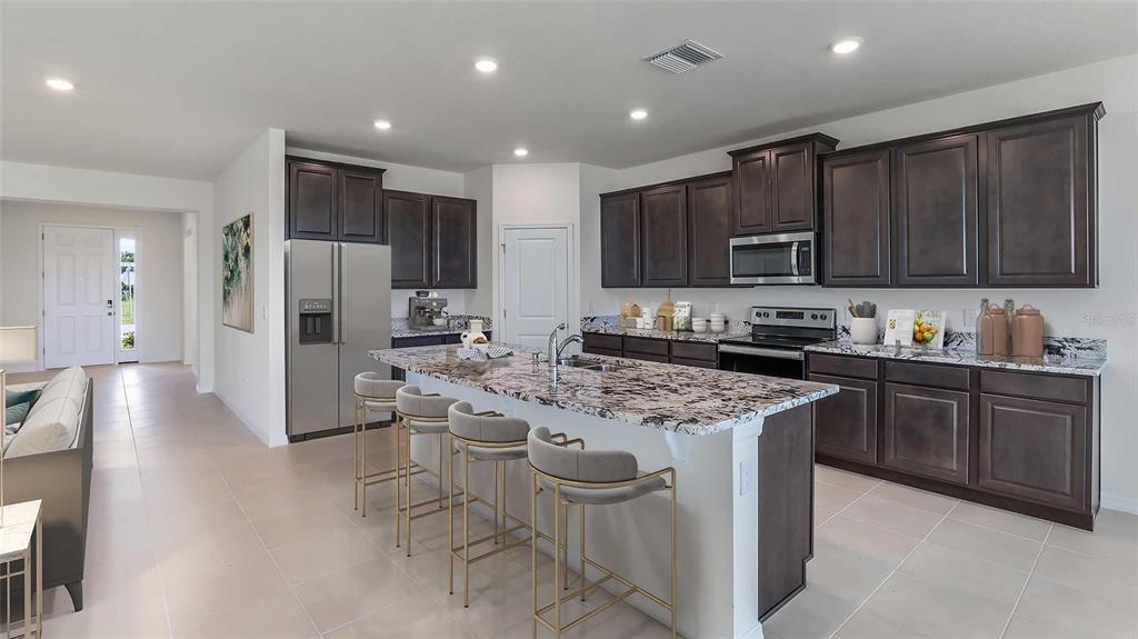 A kitchen features dark wood cabinets, granite countertops, a central island, and stainless steel appliances — 32705 DULUTH DRIVE, WESLEY CHAPEL, FL