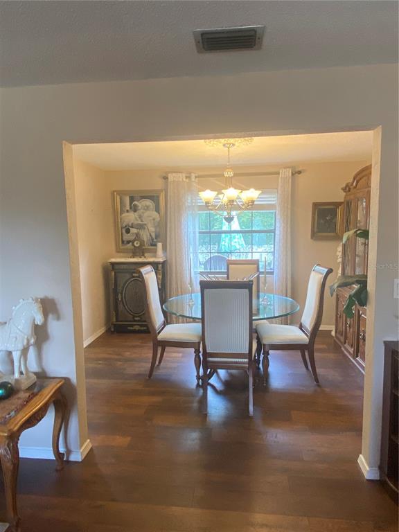 A dining room with a glass table, four chairs, a chandelier, and wood-look flooring — 1657 N NORMANDY BOULEVARD, DELTONA, FL