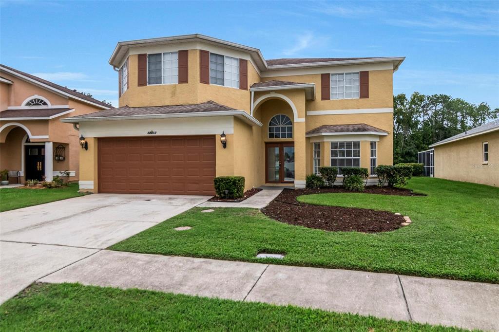 A two-story yellow stucco house with a brown garage door and a front lawn — 27512 BREAKERS DRIVE, WESLEY CHAPEL, FL
