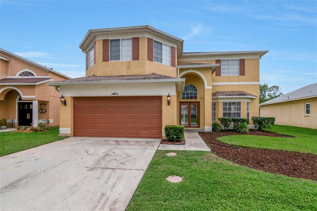 A two-story yellow stucco house with a brown garage door and a front lawn — 27512 BREAKERS DRIVE, WESLEY CHAPEL, FL