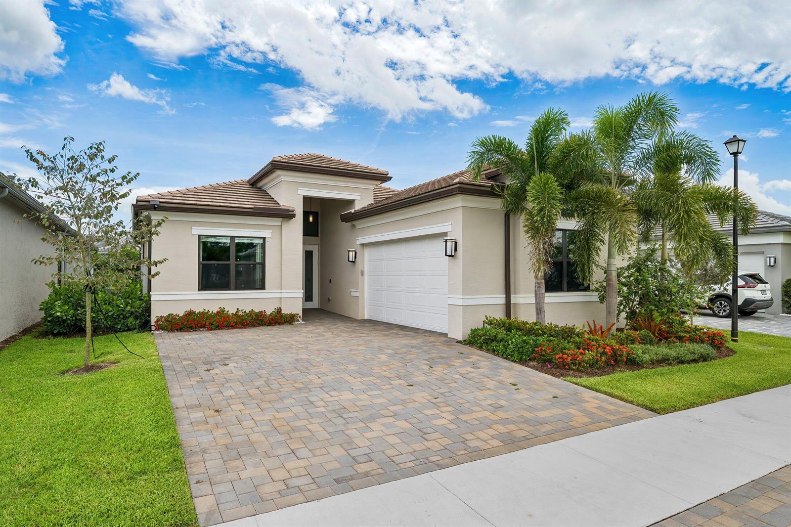 A single-story beige house with a paver driveway, two-car garage, and palm trees — 9812 Spruce Woods Drive, Boynton Beach FL 33473, BOYNTON BEACH, FL