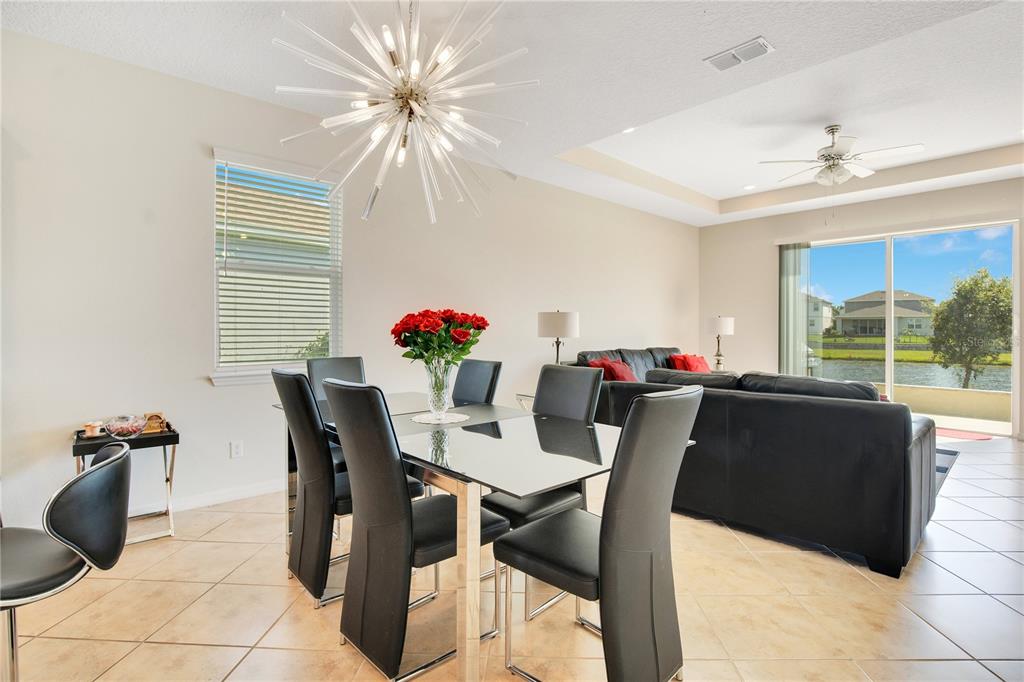 A dining area with a glass table and chandelier opens to a living room with water views — 5133 CHICKADEE STREET, ST CLOUD, FL
