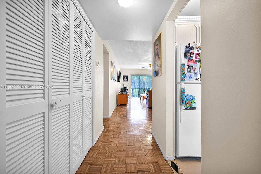 A hallway with parquet wood flooring leads toward a living area with a sliding door — 4800 Hillcrest Ln # 210, Hollywood FL 33021, HOLLYWOOD, FL