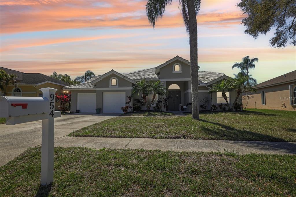 A single-story house with a two-car garage, beige stucco exterior, and a mailbox in front — 954 COBBLESTONE LANE, TARPON SPRINGS, FL
