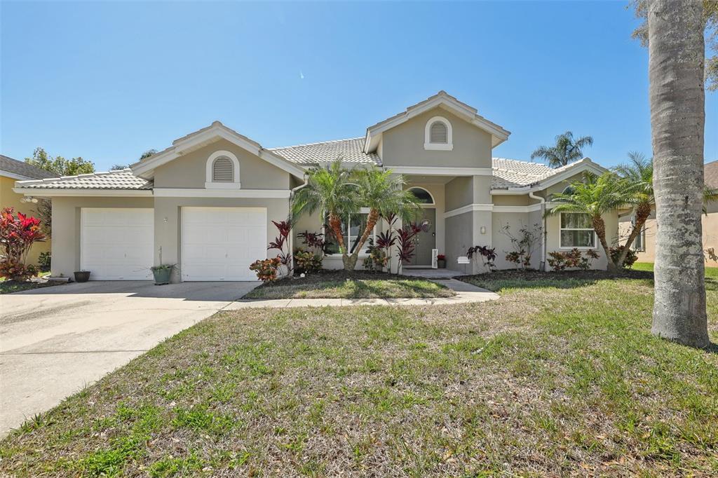A single-story house with a two-car garage, light-colored stucco walls, and a tiled roof — 954 COBBLESTONE LANE, TARPON SPRINGS, FL
