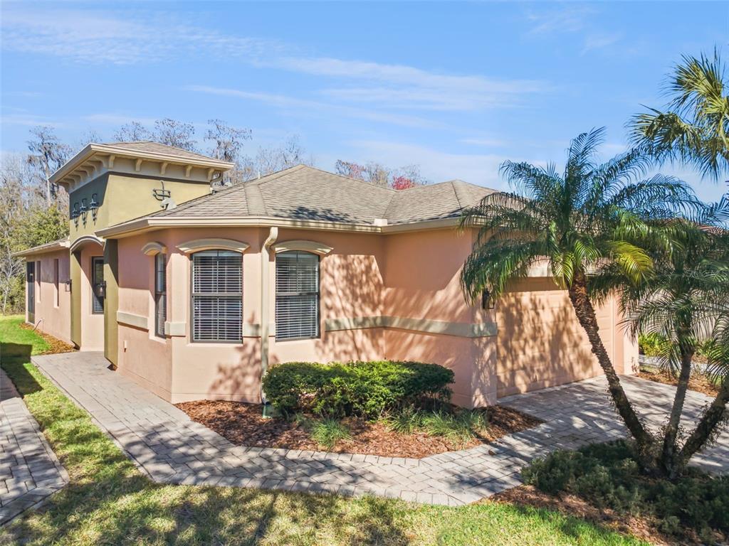 A peach-colored house with a paver driveway, a palm tree, and a small garden bed — 884 GRAND CANAL DRIVE, KISSIMMEE, FL