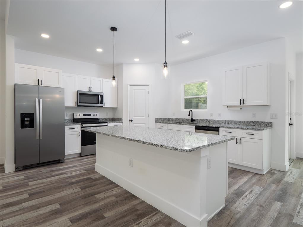 A modern kitchen features white cabinets, granite countertops, stainless steel appliances, and wood-look flooring — 217 SW 246TH WAY, NEWBERRY, FL