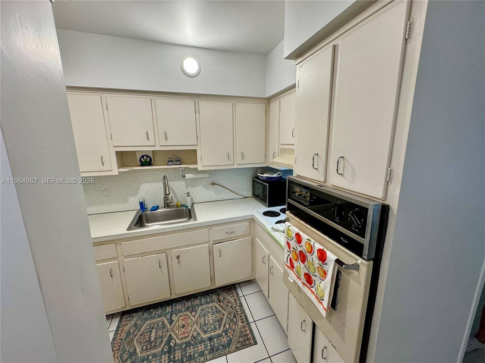 A small kitchen features off-white cabinets, a stainless steel sink, and a built-in oven — 6580 Santona St # A38, Coral Gables FL 33146, CORAL GABLES, FL