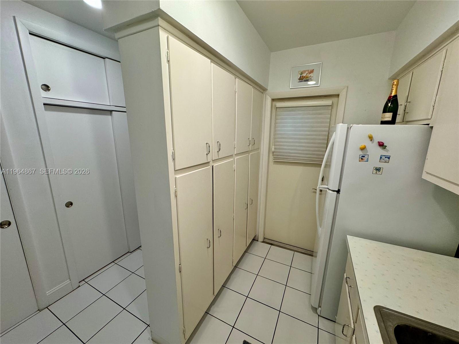 A kitchen features white cabinets, a white refrigerator, and white tile flooring — 6580 Santona St # A38, Coral Gables FL 33146, CORAL GABLES, FL