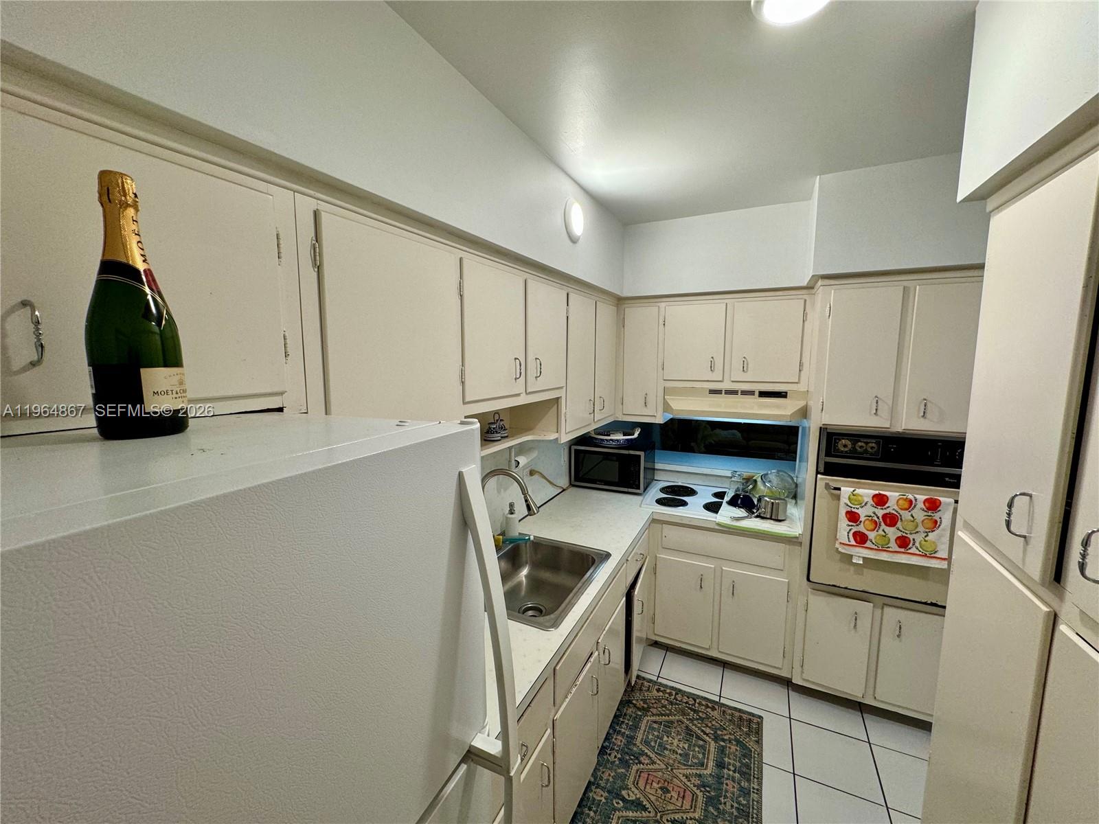 A compact kitchen features white cabinets, a stainless steel sink, and a built-in wall oven — 6580 Santona St # A38, Coral Gables FL 33146, CORAL GABLES, FL