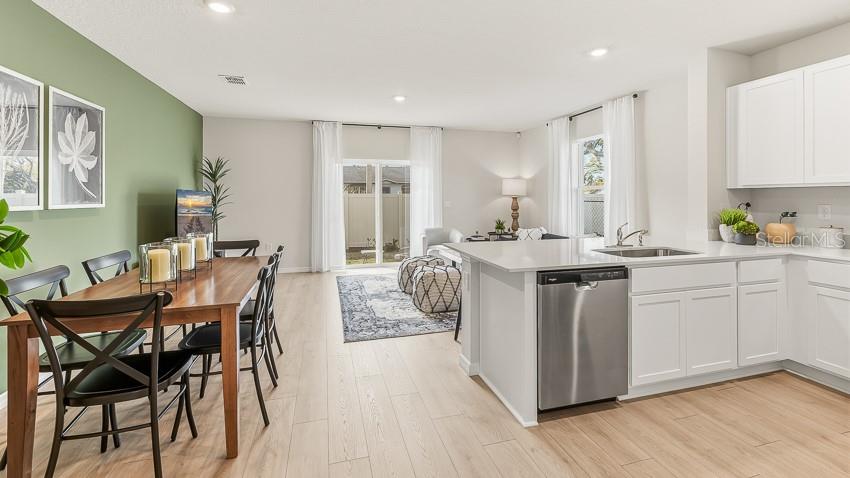 A dining area and kitchen feature light wood flooring, white cabinetry, and a green accent wall — 2120 PILSNER LOOP, BRADENTON, FL