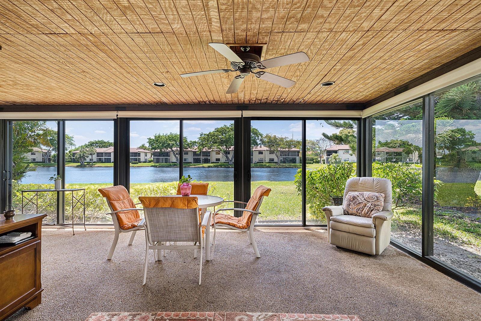 A sunroom with a wood-paneled ceiling, ceiling fan, and sliding glass doors overlooking a lake — 21875 Arriba Real # 18b, Boca Raton FL 33433, BOCA RATON, FL