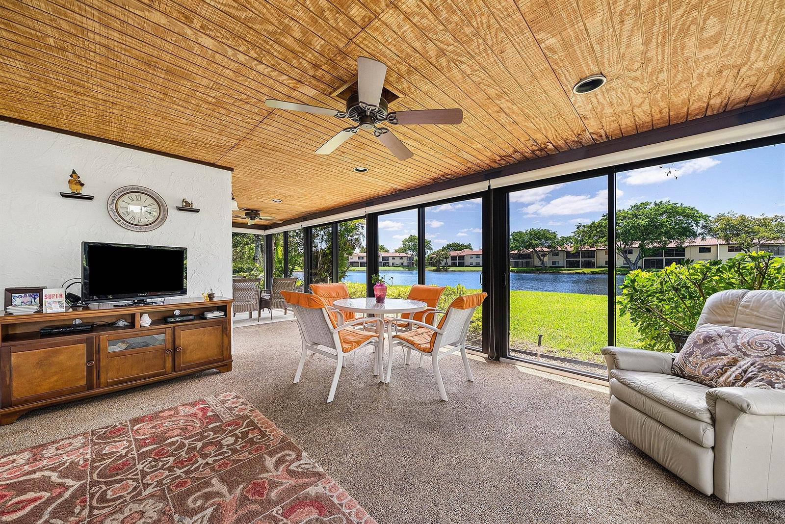 A sunroom features a wood-paneled ceiling, carpeted floors, and sliding glass doors overlooking a lake — 21875 Arriba Real # 18b, Boca Raton FL 33433, BOCA RATON, FL