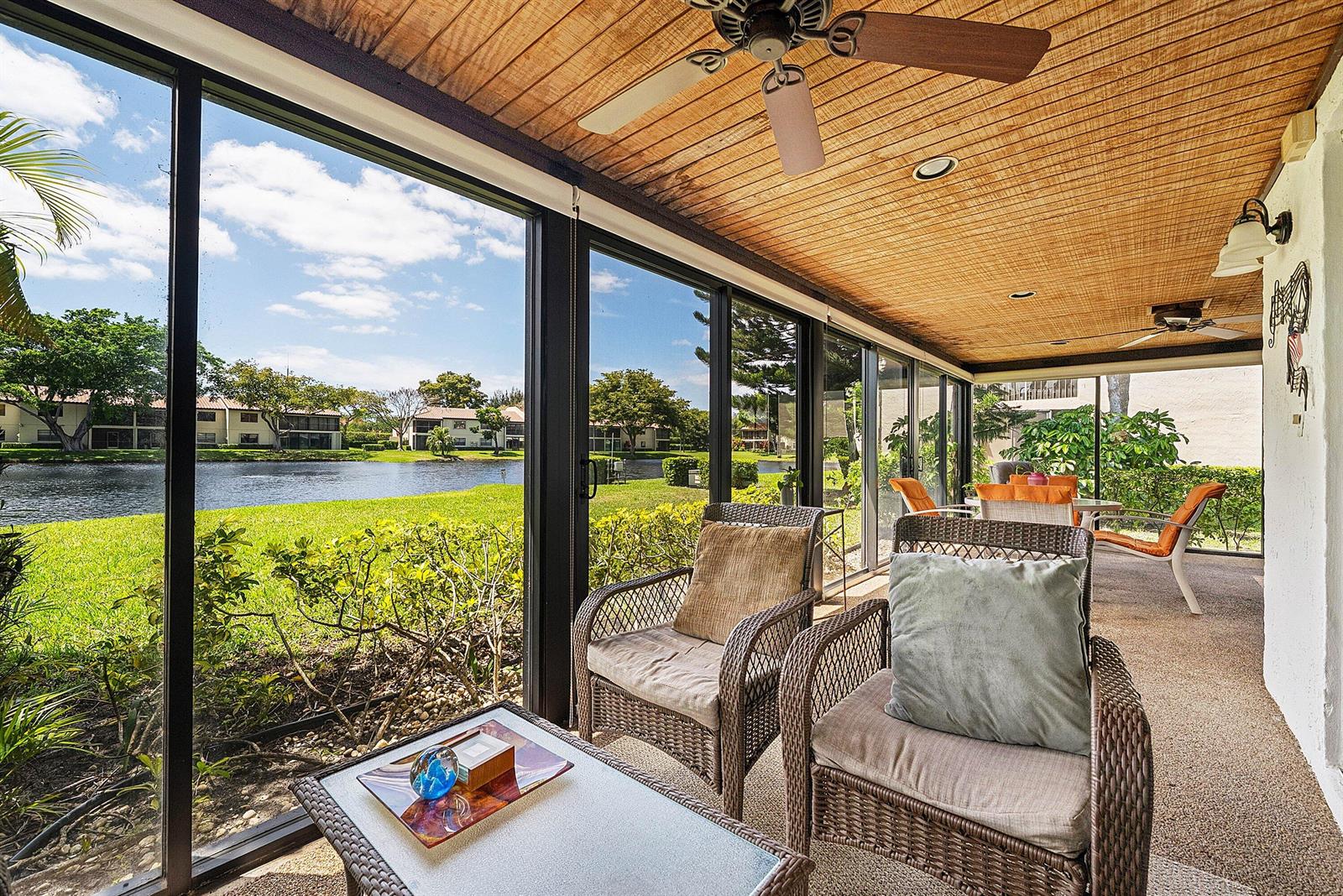 A screened-in patio with wicker furniture overlooks a lake and residential buildings — 21875 Arriba Real # 18b, Boca Raton FL 33433, BOCA RATON, FL
