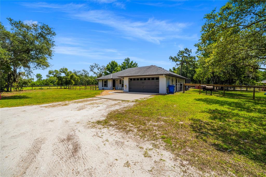 A single-story house with a gray garage door sits on a grassy lot with trees — 135 LINDA SUE DRIVE, LAKE HELEN, FL