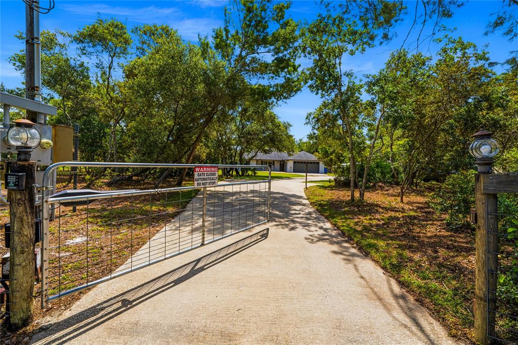 A metal gate stands across a concrete driveway leading to a house among trees — 135 LINDA SUE DRIVE, LAKE HELEN, FL