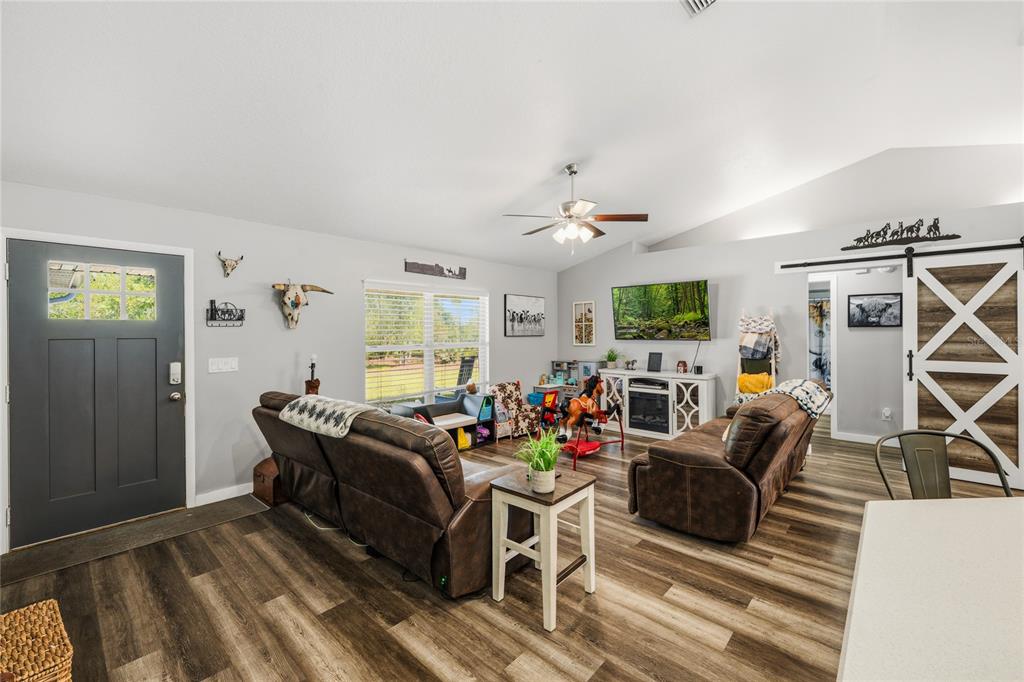 A living room features wood-look flooring, two brown leather sofas, and a sliding barn door — 135 LINDA SUE DRIVE, LAKE HELEN, FL