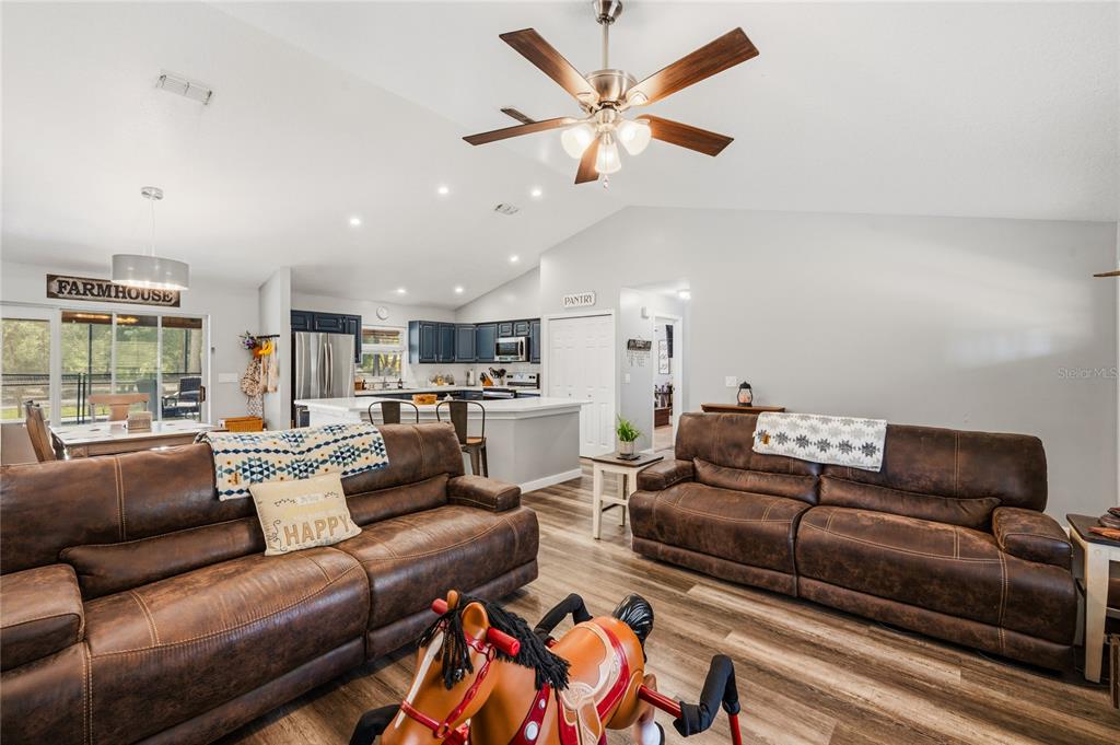 A living room with brown leather sofas, wood-look flooring, and an open-concept kitchen — 135 LINDA SUE DRIVE, LAKE HELEN, FL