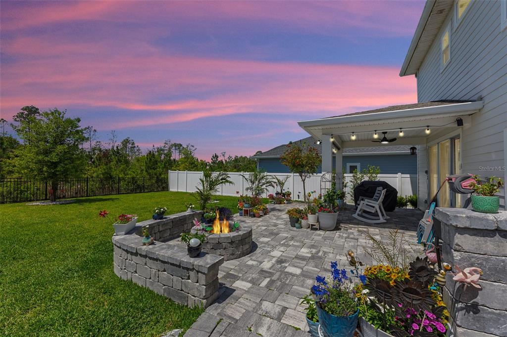 A backyard patio features a stone fire pit, paver flooring, and a covered seating area — 121 NIGHTHAWK LANE, PALM COAST, FL