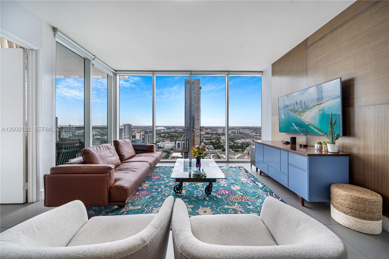 A modern living room features floor-to-ceiling windows, a brown leather sofa, and a city view — 1040 Biscayne Blvd # 3607, Miami FL 33132, MIAMI, FL