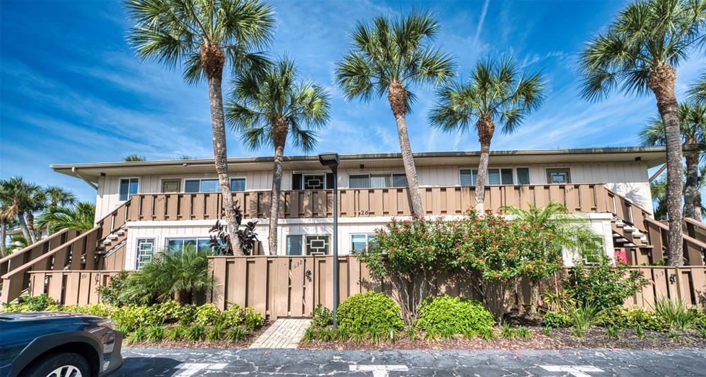 A two-story apartment building with a wooden balcony, palm trees, and a privacy fence — 6701 GULF OF MEXICO DRIVE UNIT 332, LONGBOAT KEY, FL