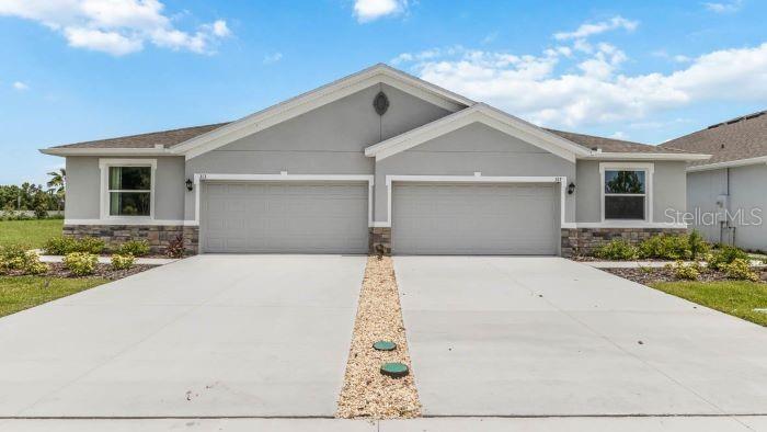 A duplex house with two garage doors and a stone-accented exterior under a blue sky — 18315 TAVERNSIDE TRAIL, LAKEWOOD RANCH, FL
