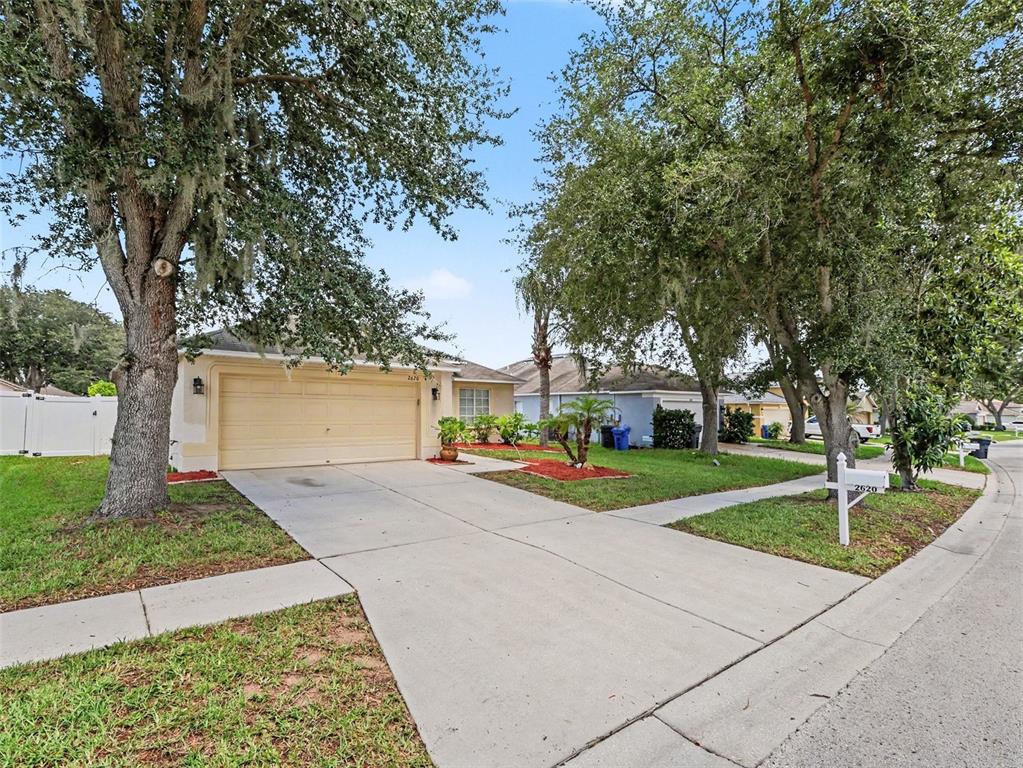 A single-story house with a beige garage and a concrete driveway under large trees — 2620 BUCKHORN PRESERVE BOULEVARD, VALRICO, FL