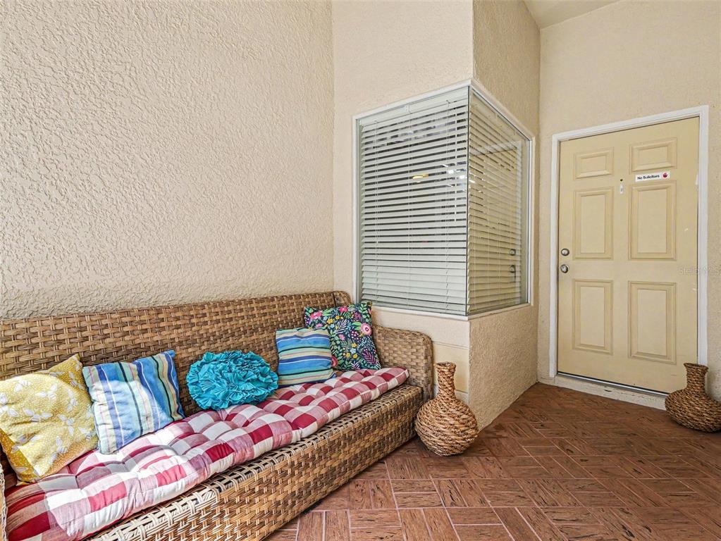 A covered patio features a wicker sofa with colorful pillows, tiled flooring, and a door — 2620 BUCKHORN PRESERVE BOULEVARD, VALRICO, FL