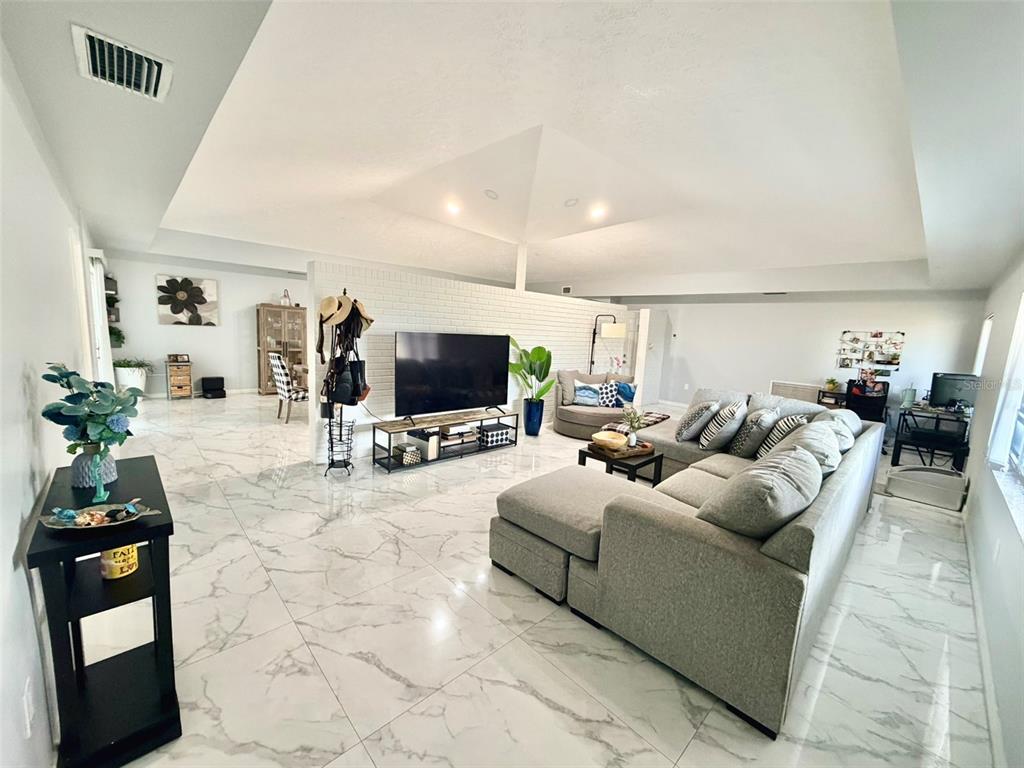 A spacious living room features large white marble-look floor tiles and a white brick wall — 6004 MEMORIAL HIGHWAY, TAMPA, FL