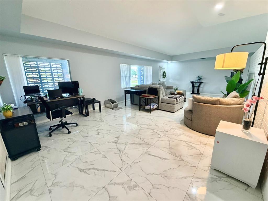 A spacious living room features white marble-look tile flooring, a home office area, and furniture — 6004 MEMORIAL HIGHWAY, TAMPA, FL