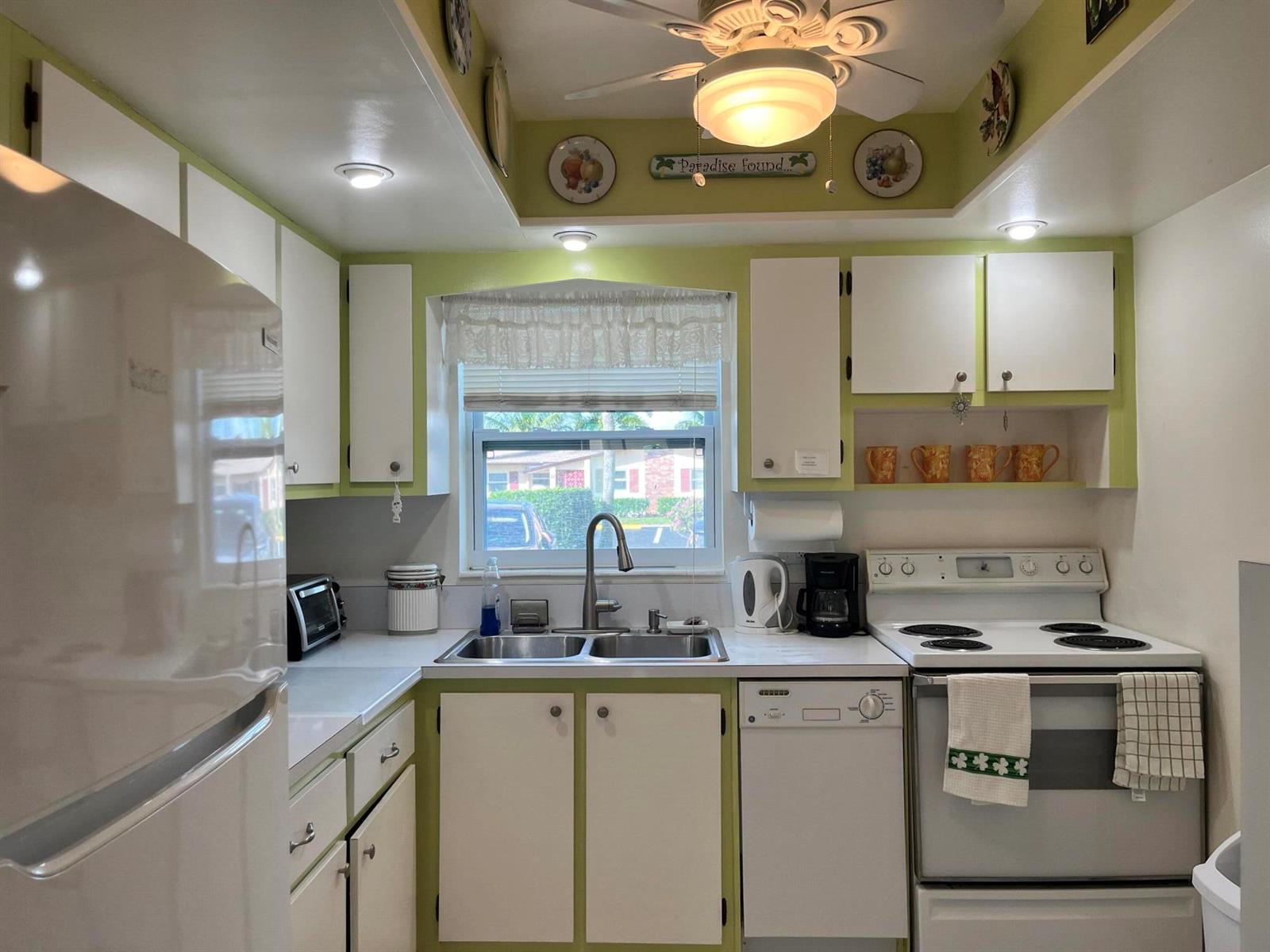 A kitchen features white cabinets, light green walls, a double sink, and a white stove — 2980 Crosley Drive E # F, West Palm Beach FL 33415, WEST PALM BEACH, FL