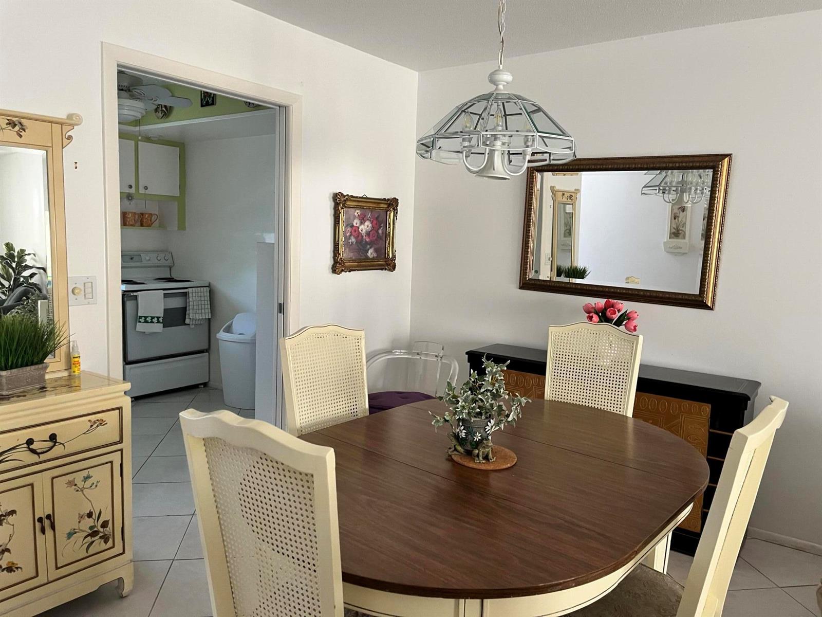 A dining room features a round wooden table, four chairs, a chandelier, and a wall mirror — 2980 Crosley Drive E # F, West Palm Beach FL 33415, WEST PALM BEACH, FL