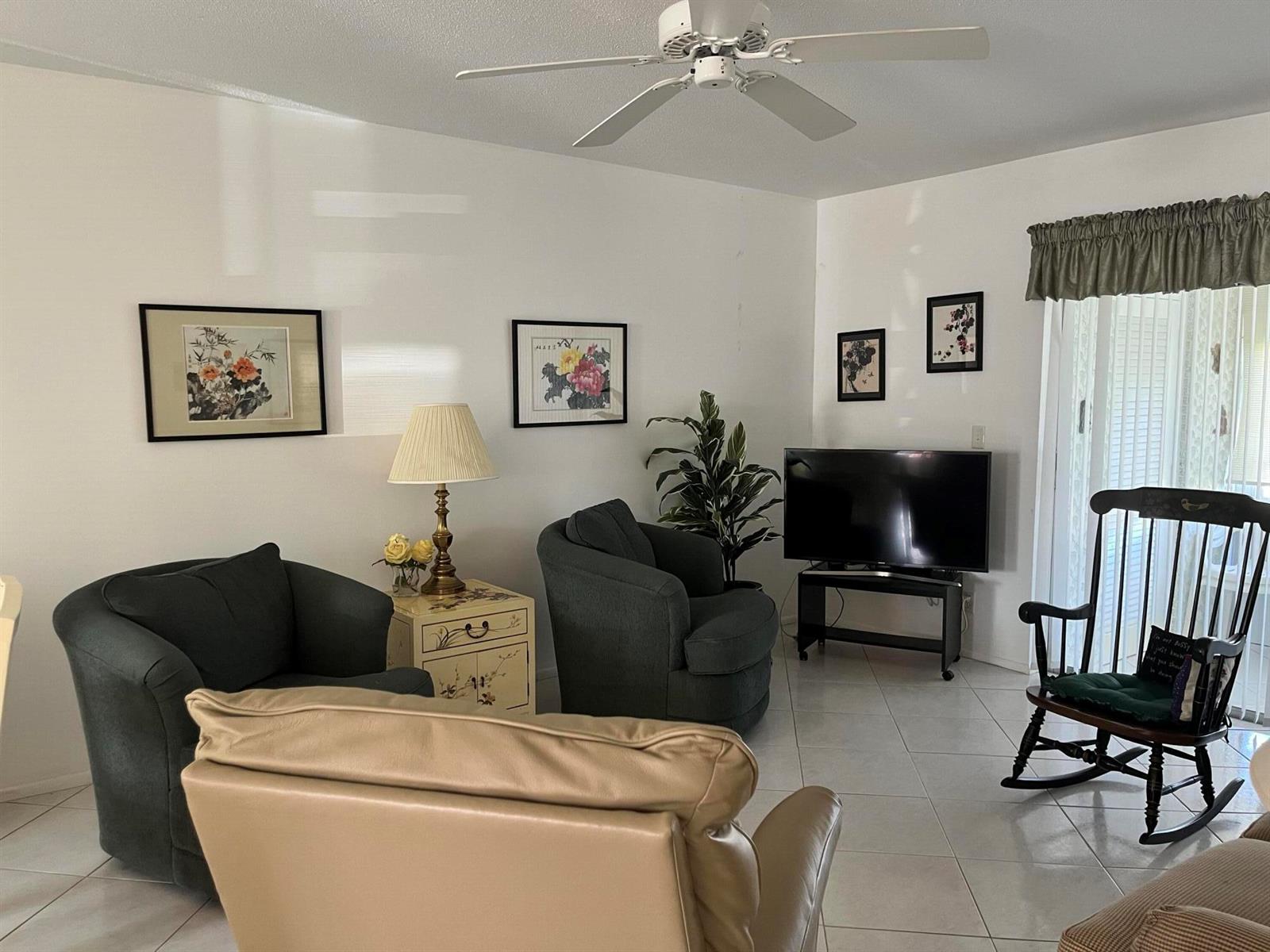 A living room features tiled floors, a ceiling fan, two dark armchairs, and a television — 2980 Crosley Drive E # F, West Palm Beach FL 33415, WEST PALM BEACH, FL