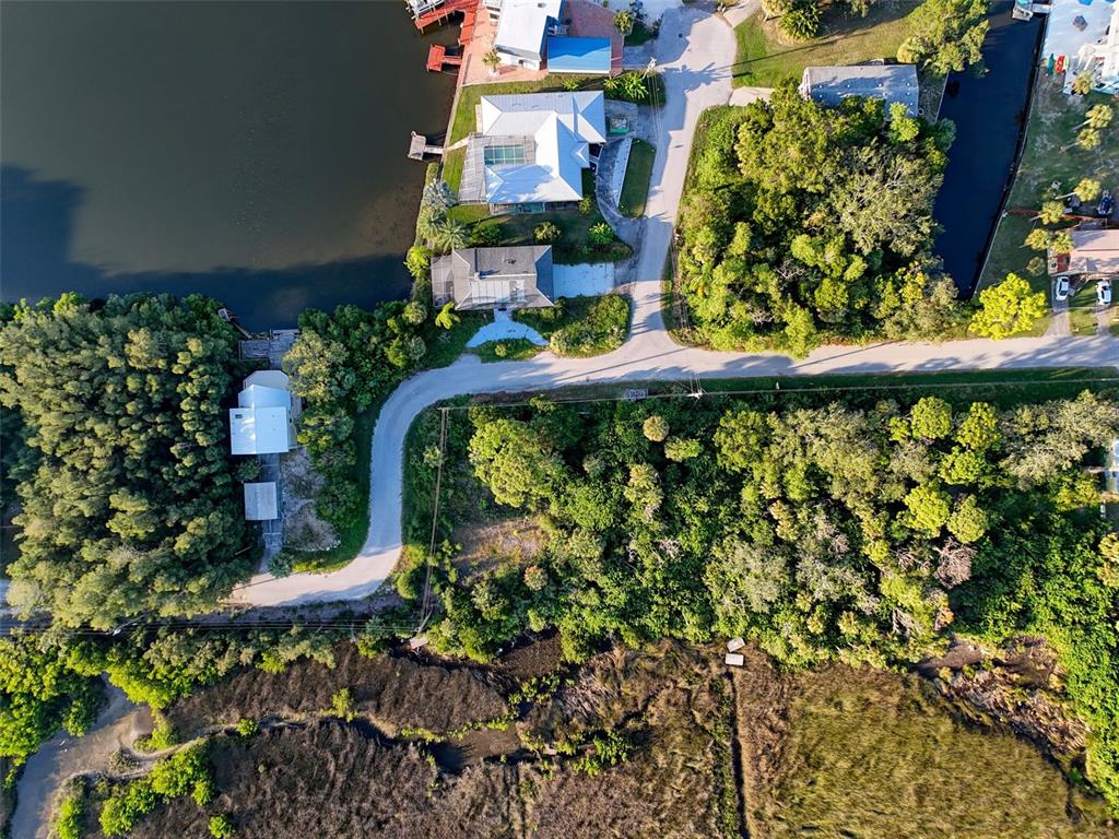 An aerial view shows a residential street, waterfront homes, and dense vegetation near a marsh — lot 12 NOWIKI AVENUE, HUDSON, FL