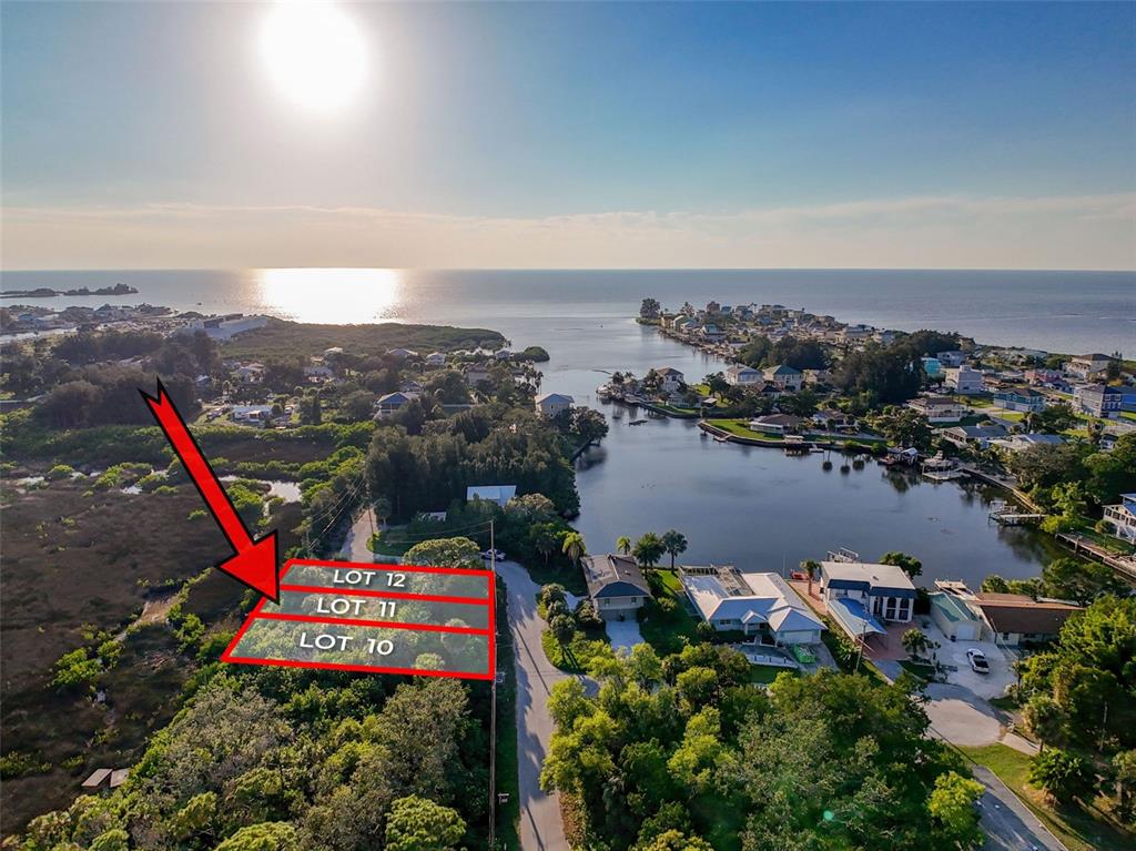 An aerial view shows three adjacent vacant lots outlined in red near a coastal waterway — lot 12 NOWIKI AVENUE, HUDSON, FL