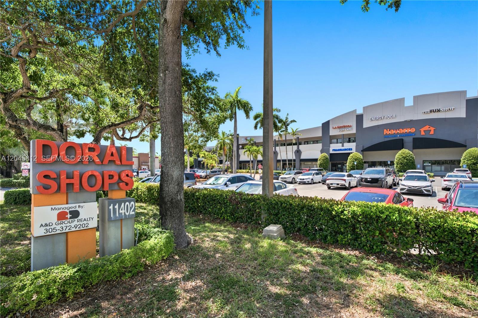 A sign for Doral Shops stands in front of a commercial plaza with parked cars — 11402 NW 41st St # 207, Doral FL 33178, DORAL, FL