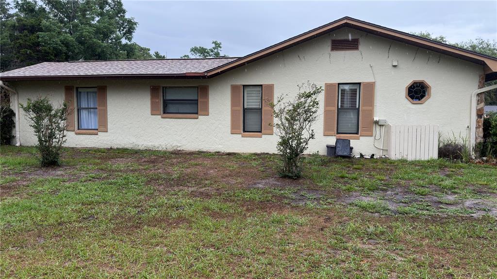 The exterior of a single-story house with beige stucco walls, brown shutters, and a lawn — 4076 S OAKHURST DRIVE, HOMOSASSA, FL