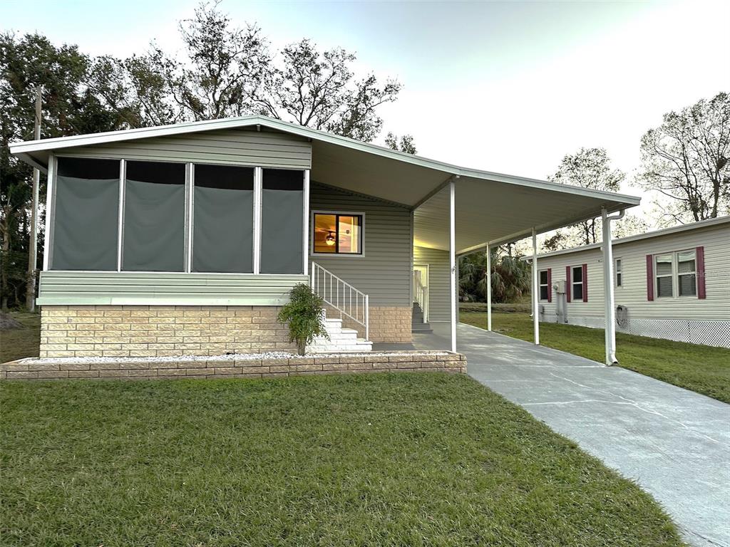 A light green manufactured home features a front sunroom, a carport, and a concrete driveway — 168 BEECHWOOD DRIVE UNIT 67, SAFETY HARBOR, FL