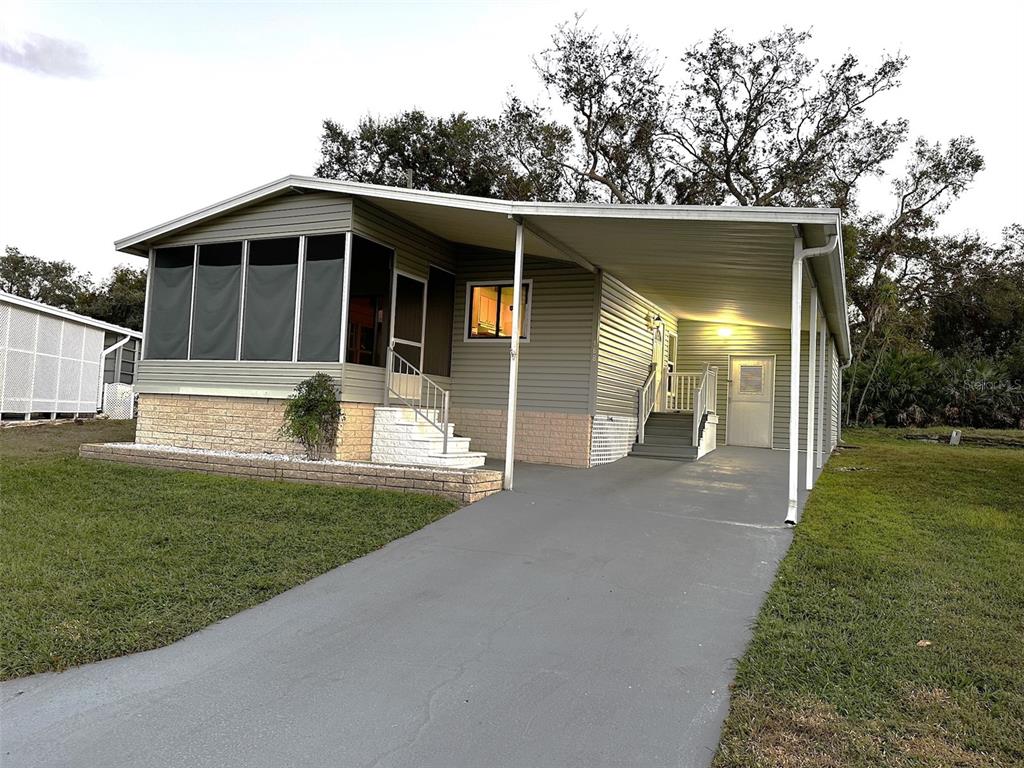 The exterior of a mobile home features light green siding, two sets of stairs, and a carport — 168 BEECHWOOD DRIVE UNIT 67, SAFETY HARBOR, FL