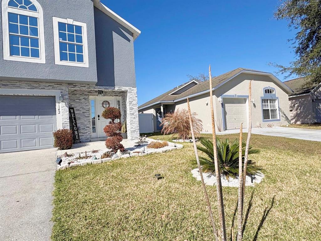 A two-story house with a gray exterior and stone accents stands next to a single-story home — 3142 WHISPERING TRAILS STREET, WINTER HAVEN, FL