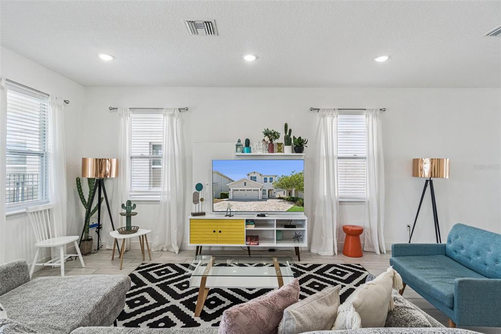 A living room features a television on a yellow and white stand with patterned rugs — 276 SOUTHFIELD STREET, KISSIMMEE, FL