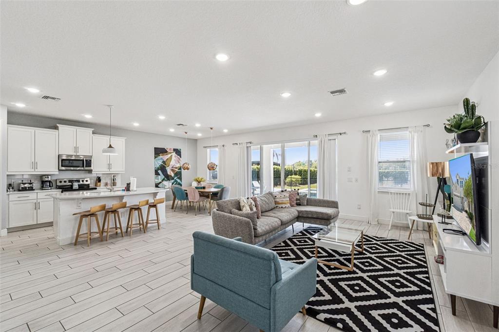 An open-concept living room and kitchen featuring white cabinetry, tile flooring, and a patterned rug — 276 SOUTHFIELD STREET, KISSIMMEE, FL